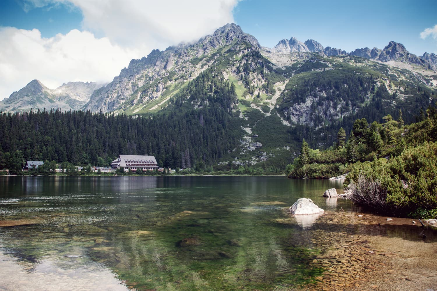 Clear green water of Popradské pleso with the mountain hotel and peaks behind