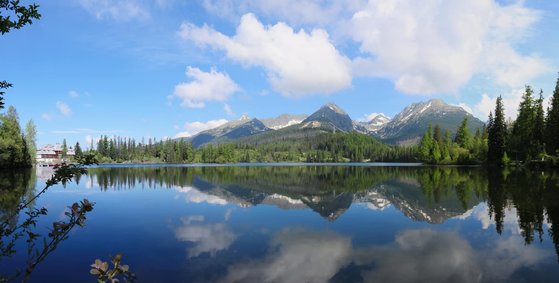 Štrbské pleso on a calm summer day with the High Tatra peaks and clouds reflected in the lake