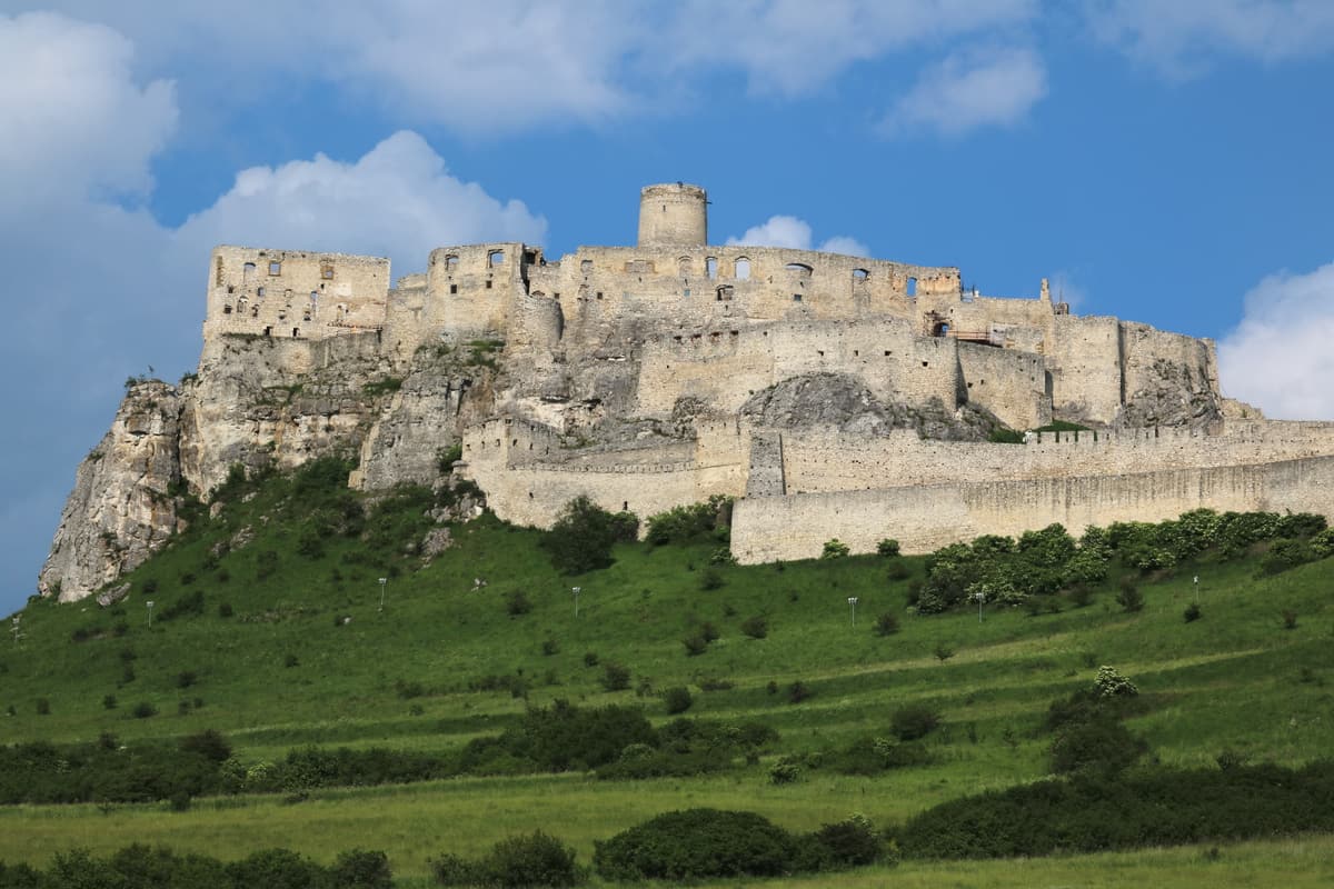 The white limestone walls of Spiš Castle on its hill above green meadows